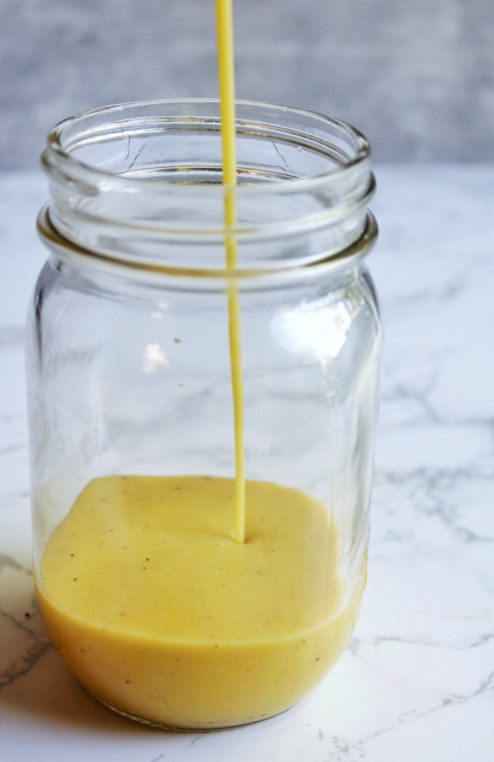 Pouring apple cider vinaigrette into a glass jar.