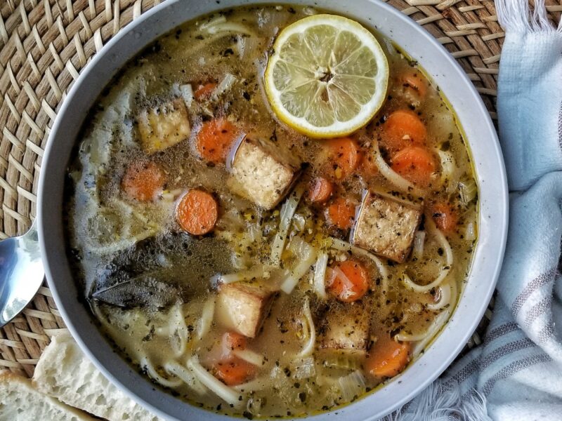 Vegan chicken noodle soup in a bowl with a slice of lemon.