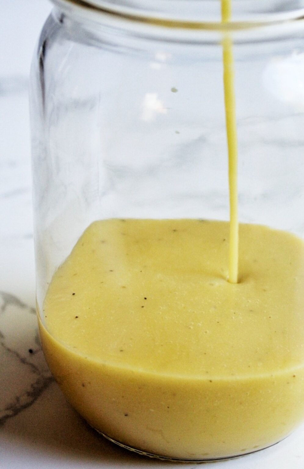 Salad dresssing being poured into a mason jar, close-up.