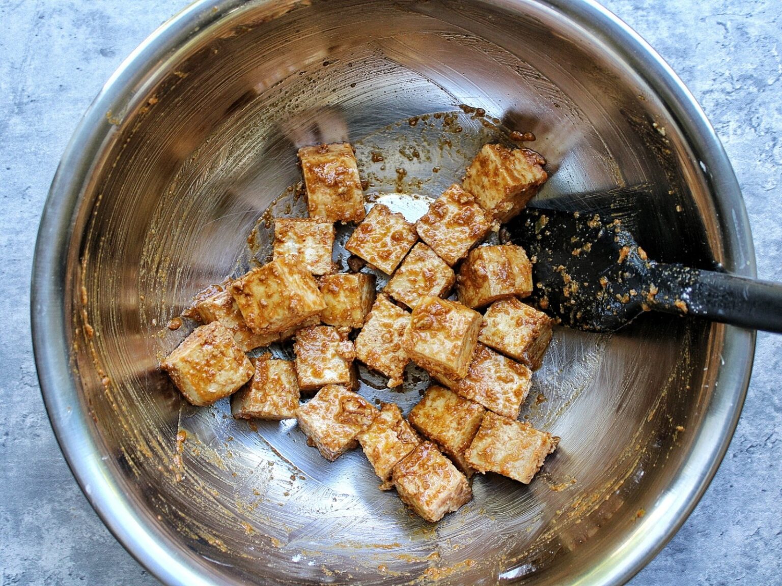 Tofu chunks in a mixing bowl with spices, soy sauce, and oil. 