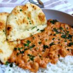 Chickpea curry in a bowl, topped with chopped cilantro. Served with rice and naan.