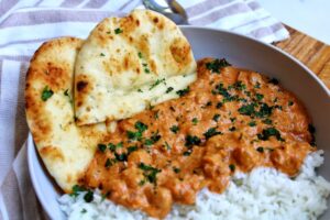 Chickpea curry in a bowl, topped with chopped cilantro. Served with rice and naan.