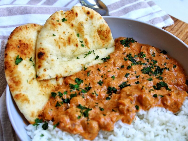 Chickpea curry in a bowl, topped with chopped cilantro. Served with rice and naan.
