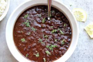 Cooked black beans topped with cilantro, garnished with lemon and a side of rice.