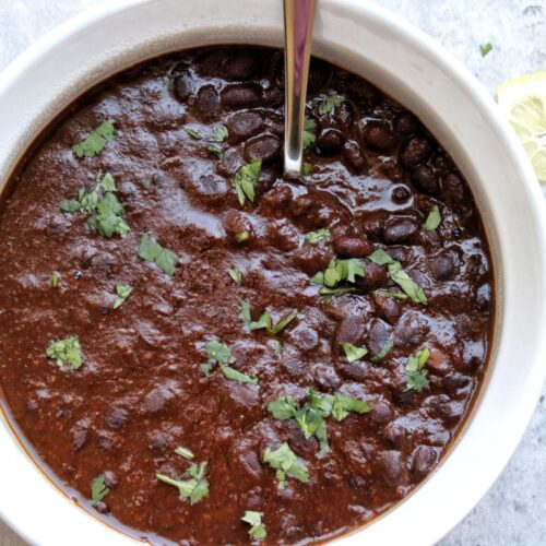 Cooked black beans topped with cilantro, garnished with lemon and a side of rice.