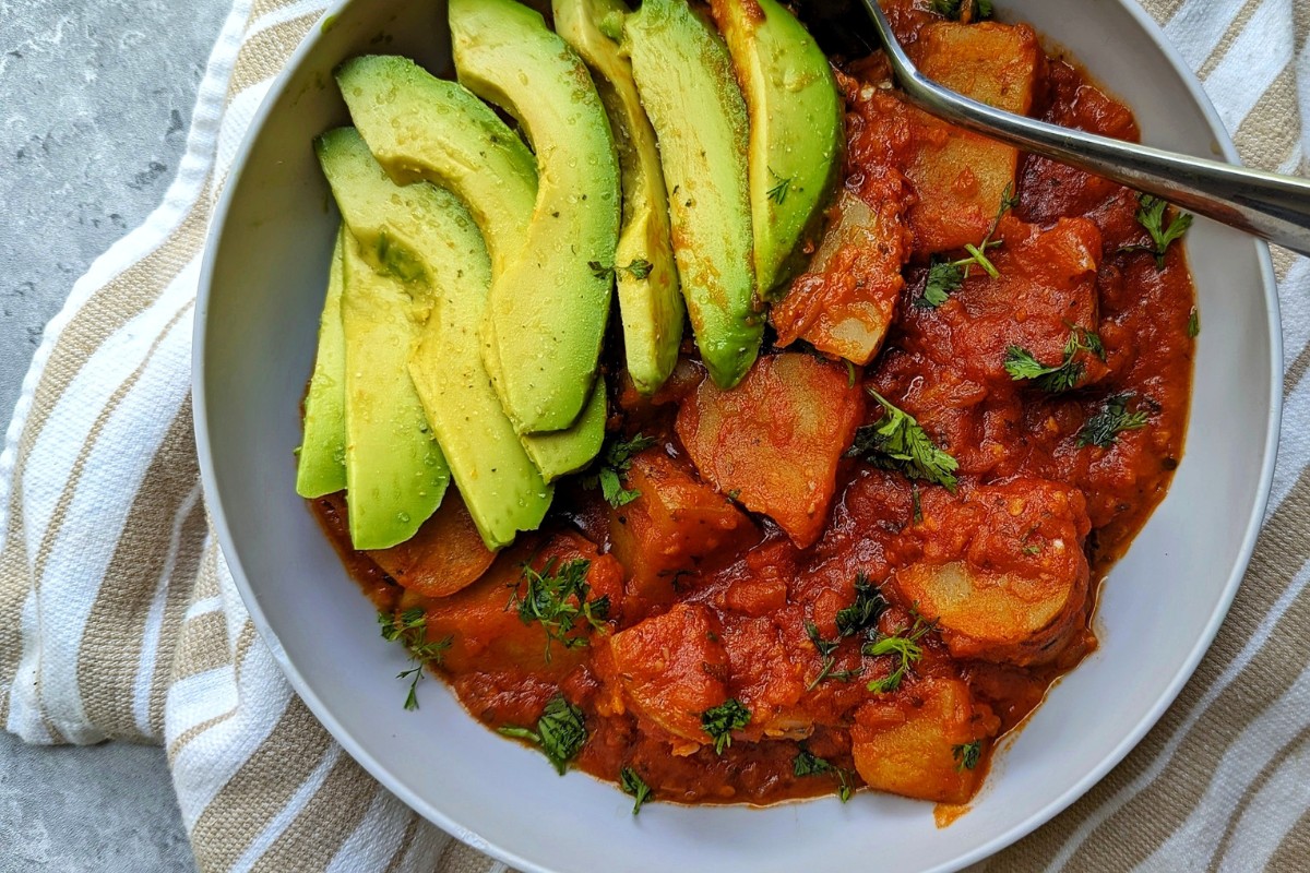 Potatoes stewed in a tomato sauce with a side of sliced avocado. 