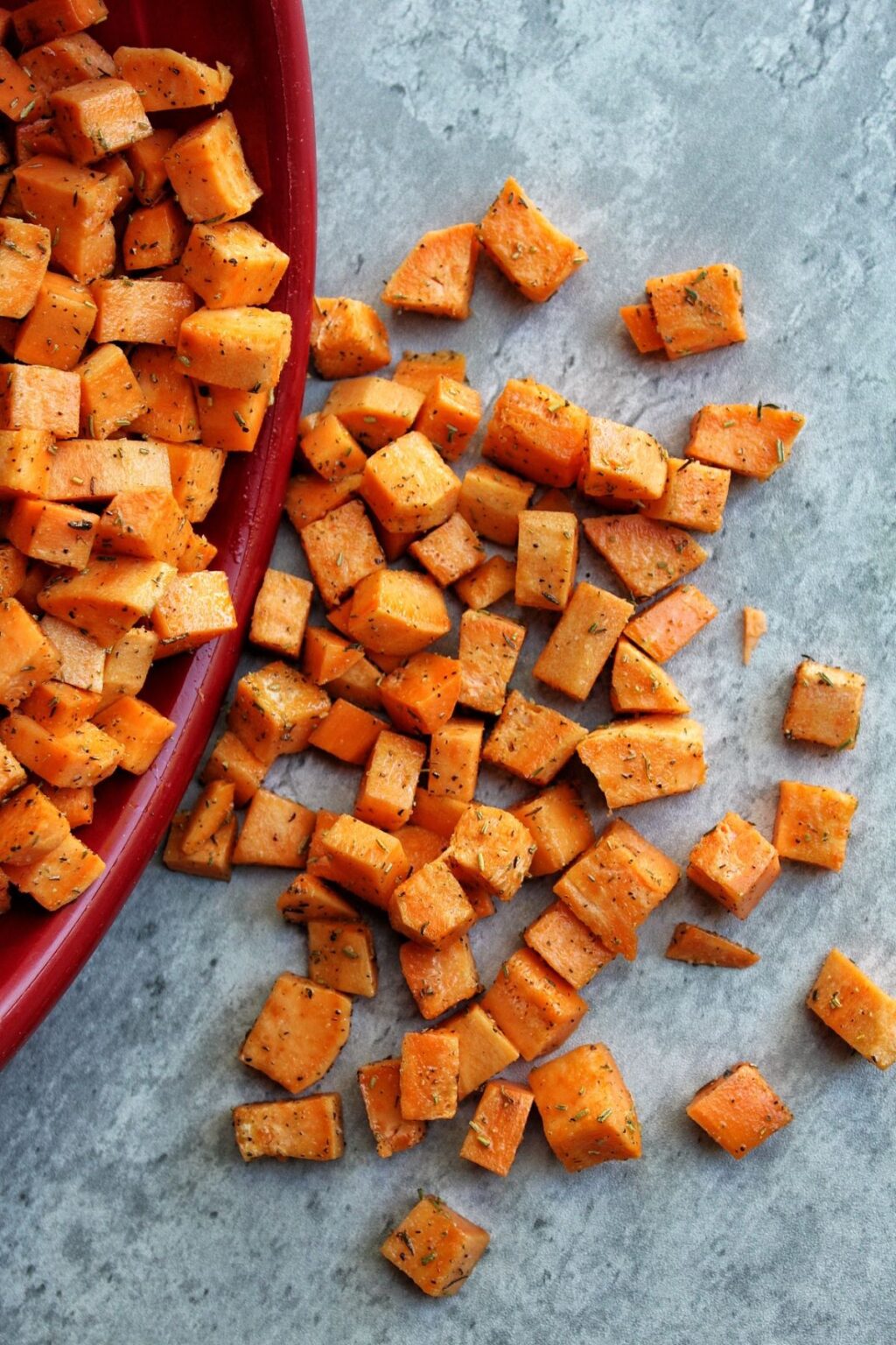 Chopped and seasoned sweet potato cubes spilling out of a red bowl.