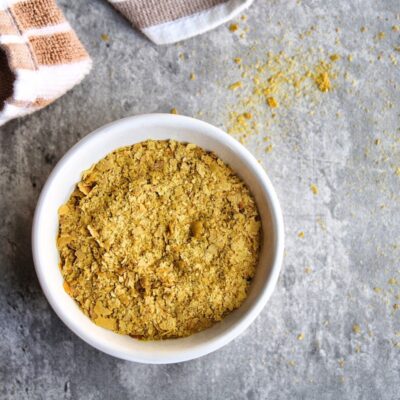 Nutritional yeast in a small bowl with a towel in the background. Horizontal view.