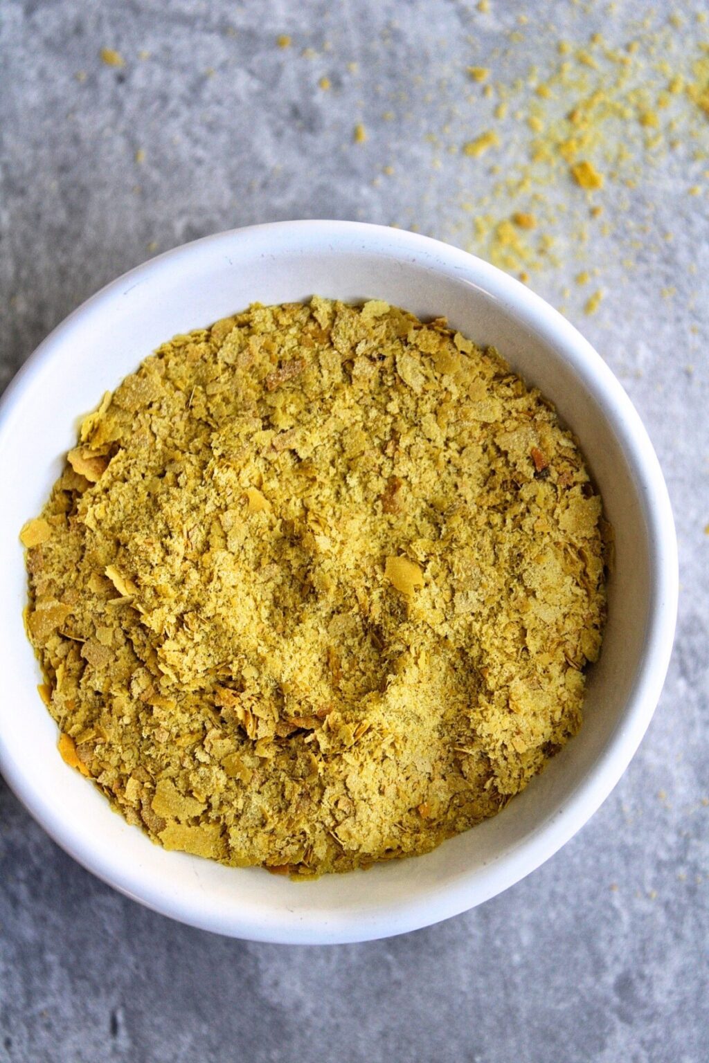 Nutritional yeast in a small bowl with a towel in the background. Vertical view.