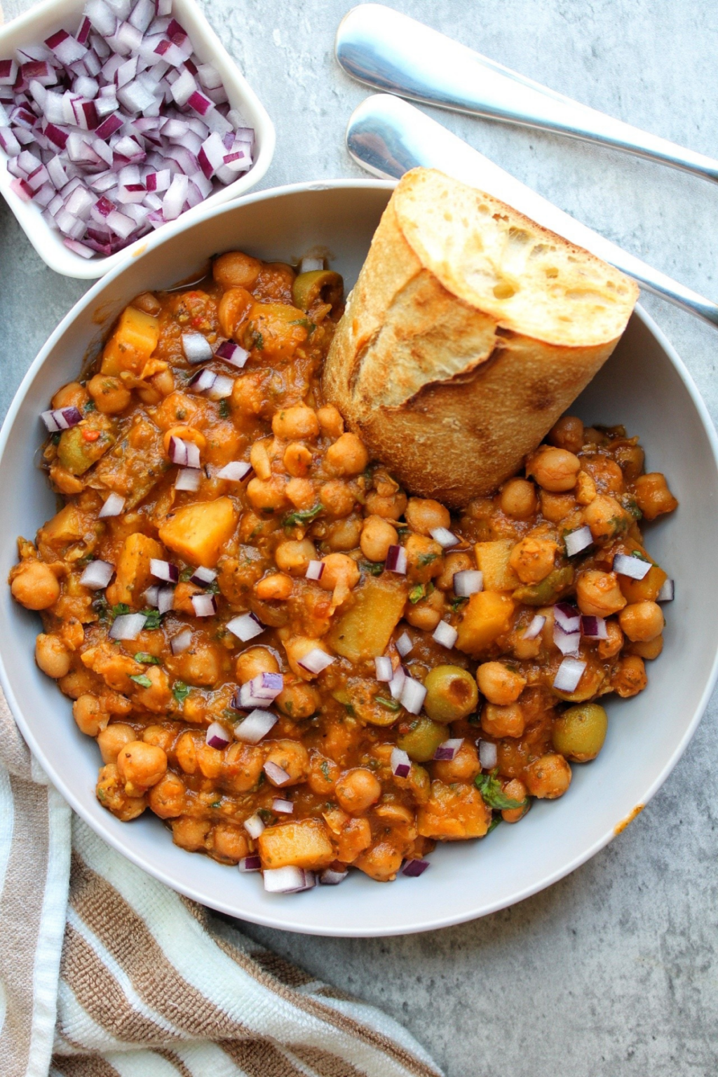 Bowl of chickpea stew topped with raw, chopped onions. 