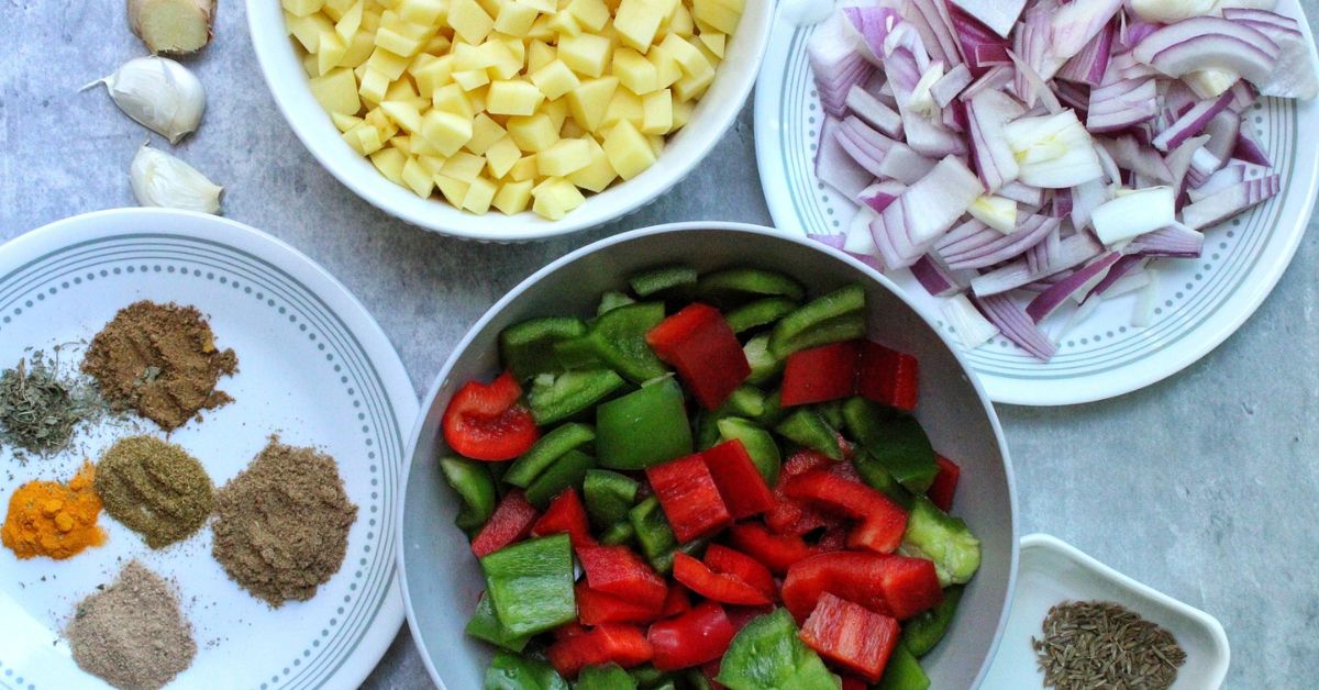 Ingredients for Aloo Capsicum including potatoes, onion, spices, bell peppers, cumin, garlic, and ginger. 