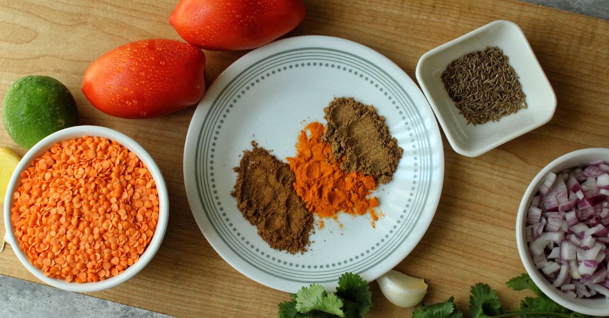 Ingredients for red lentils soup: romat tomatoes, lime, red lentils, spices, cumin, onion, garlicc, ginger, and cilantro. 