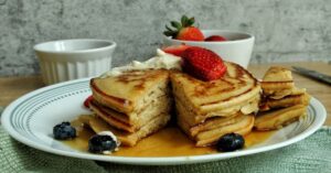 Stack of whole wheat pancakes topped with strawberries and blueberries.