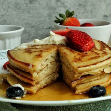 Stack of whole wheat pancakes topped with strawberries and blueberries.