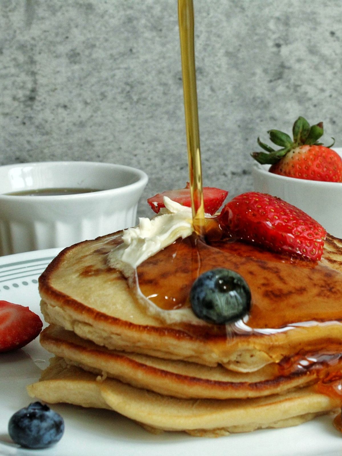 Cooked whole wheat pancakes topped with berries, vegan butter, with a syrup pour. 
