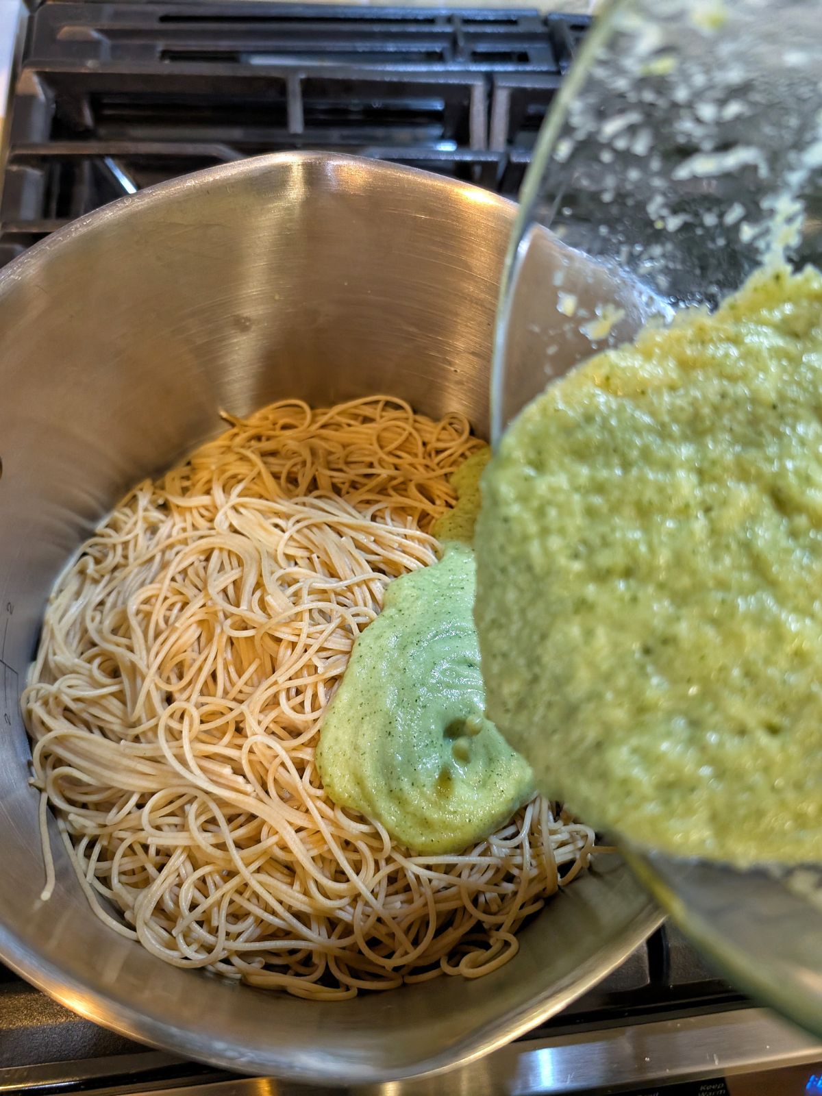 Homemade zucchini pasta sauce being poured into a pot of whole wheat pasta.