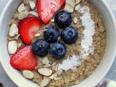 Bowl of creamy quinoa porridge topped with berries, sliced almonds, and a splash of coconut milk.
