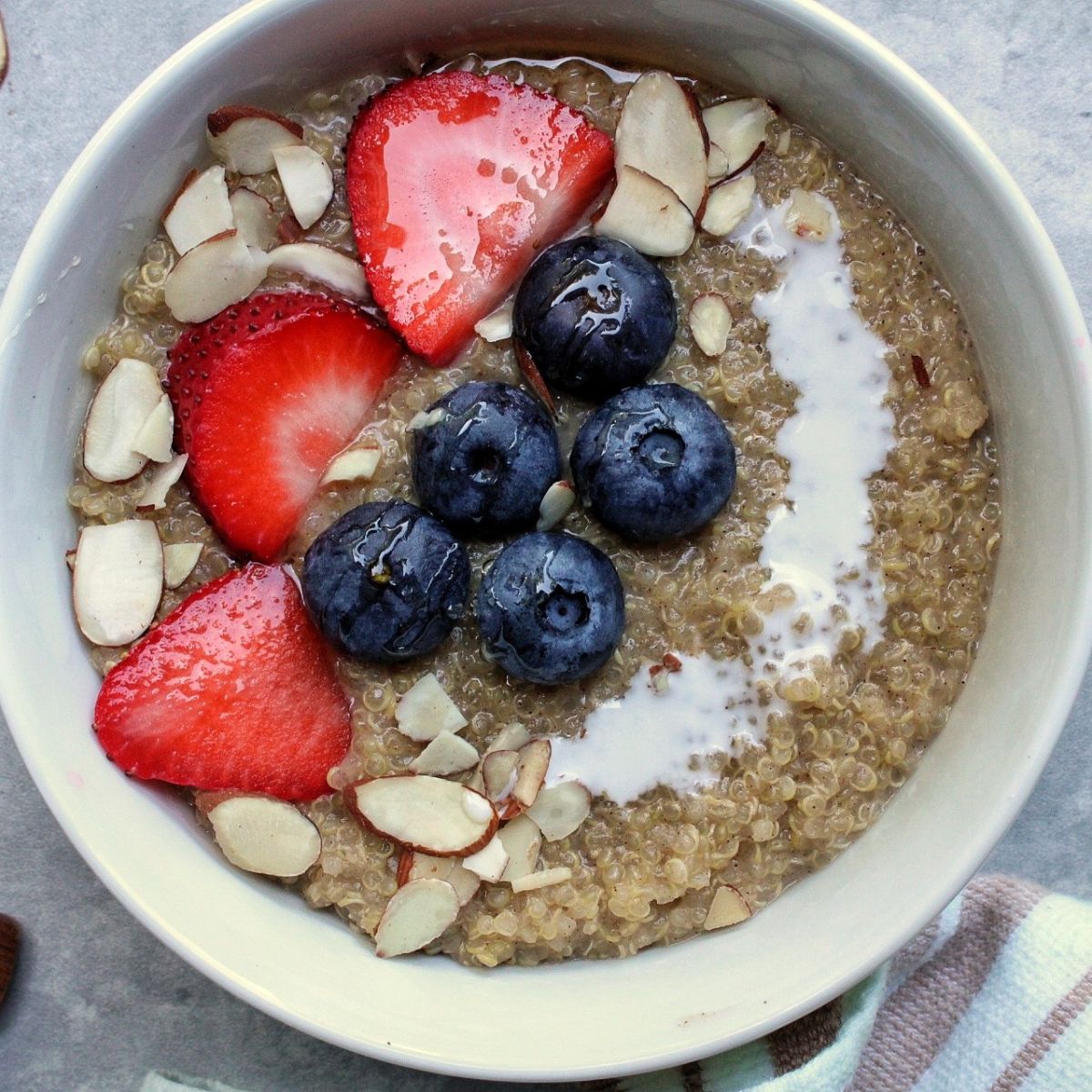 Bowl of creamy quinoa porridge topped with berries, sliced almonds, and a splash of coconut milk.