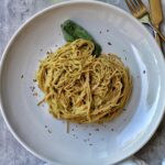 Whole wheat spaghetti with zucchini pasta sauce, basil, and red pepper flakes on a white plate.