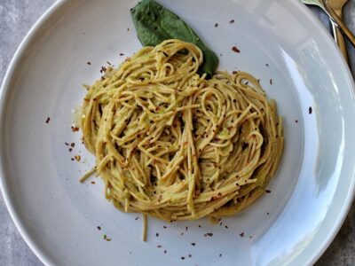 Whole wheat spaghetti with zucchini pasta sauce, basil, and red pepper flakes on a white plate.
