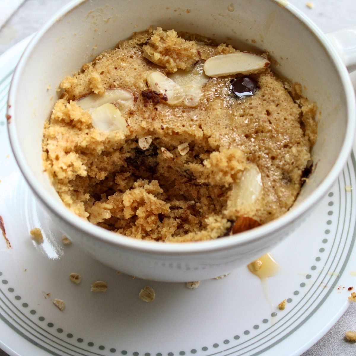 Cooked oatmeal mug cake topped with sliced almonds and maple syrup.