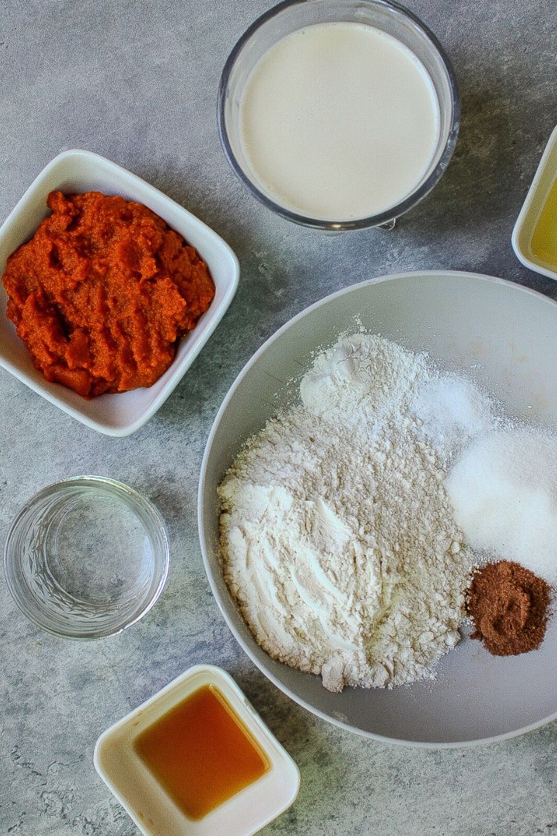 Pumpkin puree, oat milk in a glass, water, avocado oil, maple syrup, and dry ingredients in a wide bowl: flour, sugar, salt, baking powder, pumpkin pie spice. 