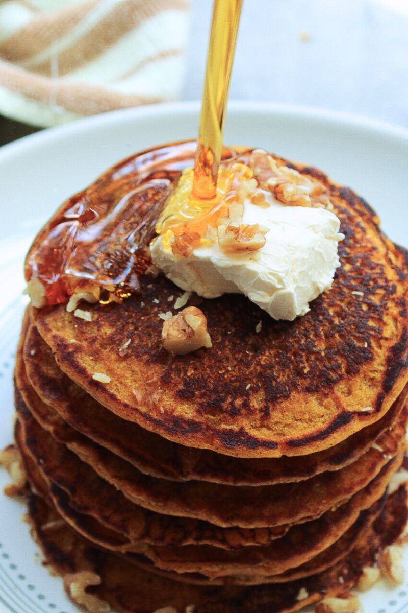 Stack of vegan pumpkin pancakes topped with a heavy pour of maple syrup, butter, and chopped walnuts. 